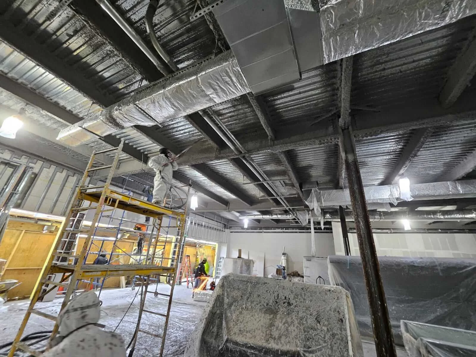 Commercial ceiling insulation project with scaffolding and a worker in protective clothing